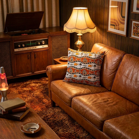 Orange and white African print pillow cover on a vintage cognac leather sofa in a wood-paneled den