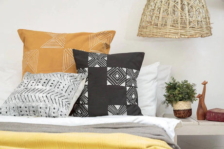 Matika black mudcloth pillow cover on a bed with a mustard pillow