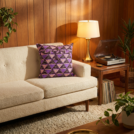 Purple African print pillow cover on a vintage cream sofa in a wood-paneled living room