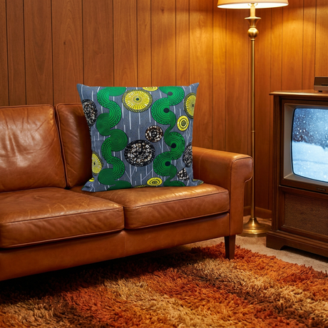 Blue and green African print pillow cover on a vintage cognac leather sofa in a wood-paneled den