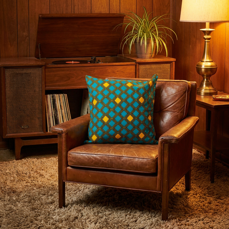 Turquoise and yellow African print pillow cover on a vintage leather armchair in a wood-paneled den