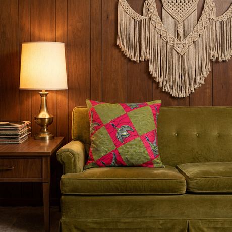 Red print African pillow cover on a vintage olive velvet sofa in a wood-paneled living room