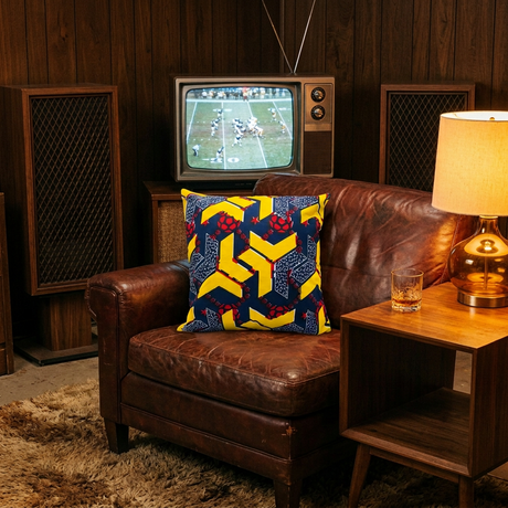 Navy and yellow African print pillow cover on a vintage leather chair in a wood-paneled den
